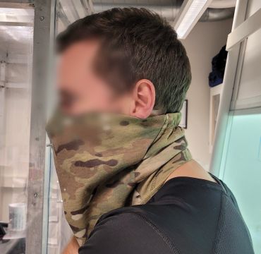 En testperson står med en SAFEgaiter kamuflasbuff med åndedrettsvern i ett av FFIs laboratorier. Ansiktet er sladdet.