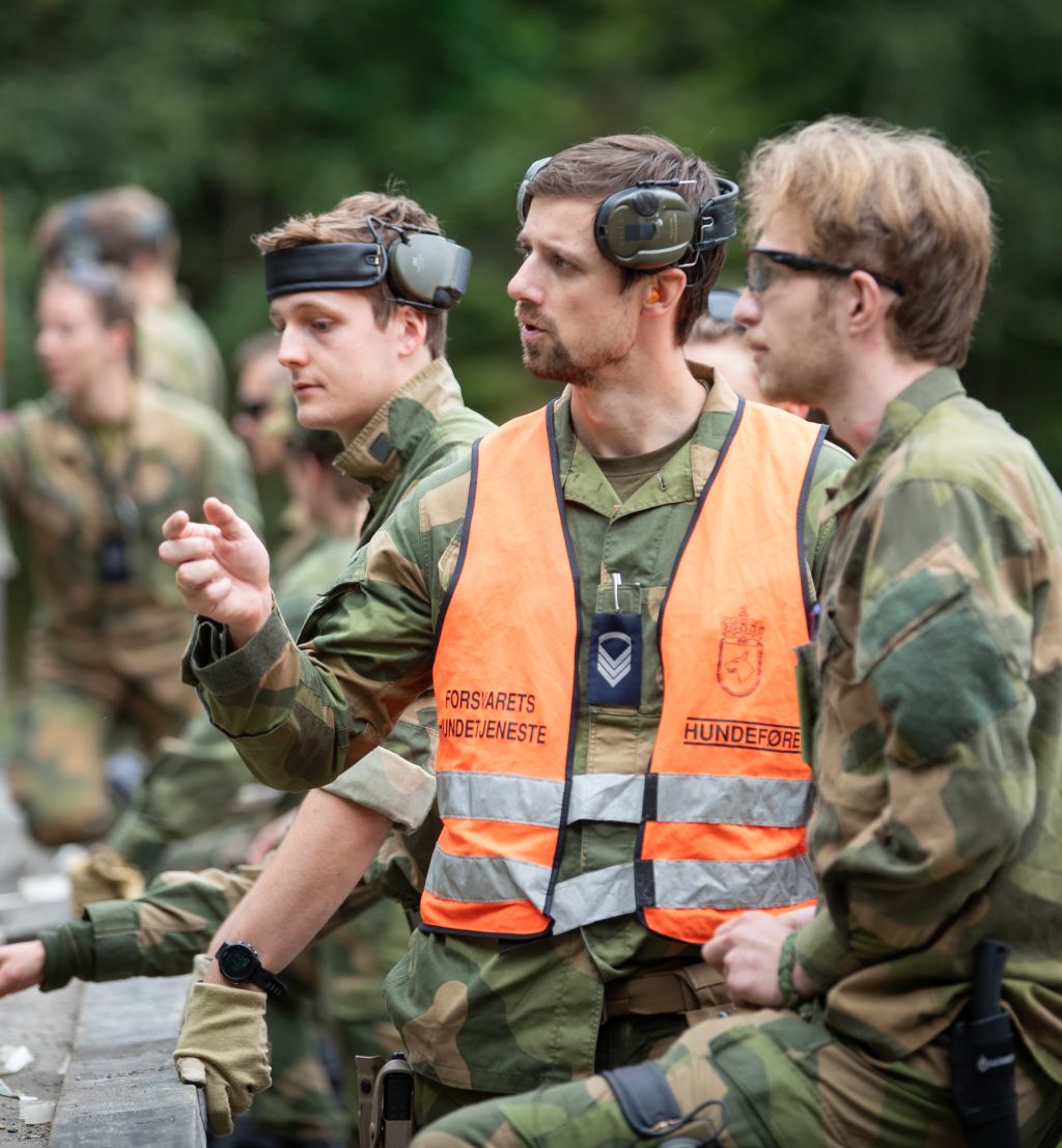 Soldater i kamuflasjeuniform på øvelse. En elev og en instruktør står og ser på noe og diskuterer.