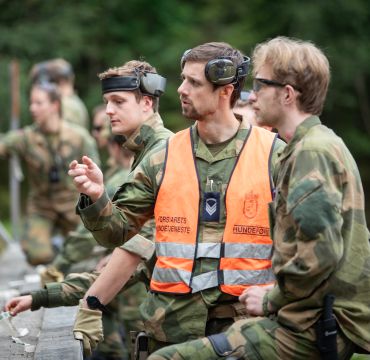 Soldater i kamuflasjeuniform på øvelse. En elev og en instruktør står og ser på noe og diskuterer.