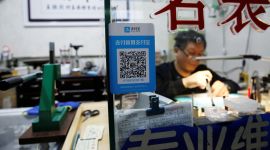 En reparatør sitter bak en pult, mens en QR-kode tydelig viser hvordan han vil ha betalt via en QR-kode og Alipay.