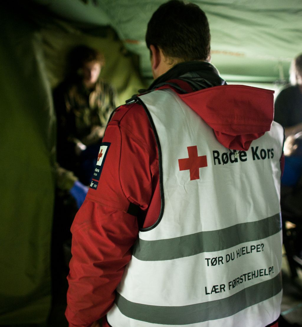 inne i et militært telt. vi ser tyggen på en med vest fra røde kors i fokus og annet militært personell rundt