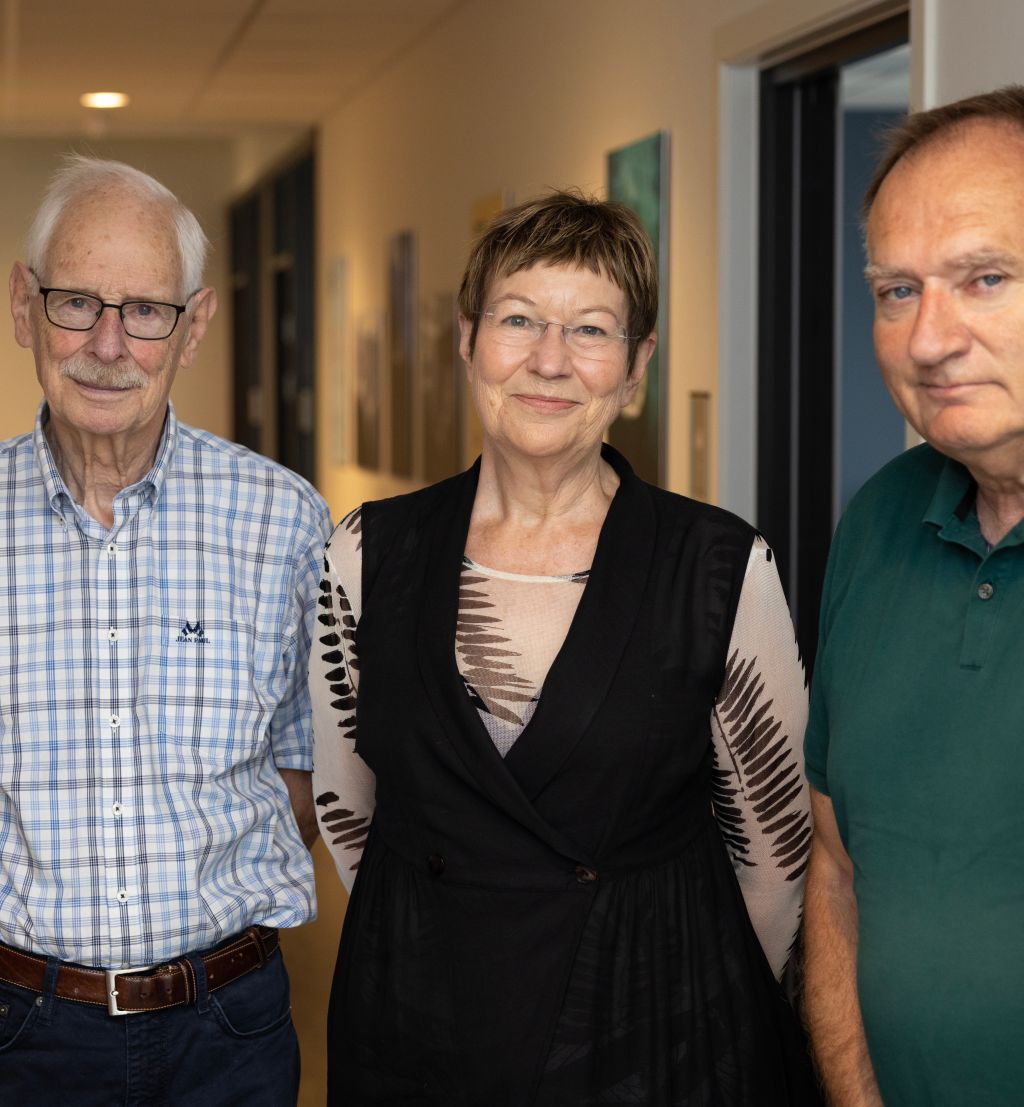 Tre eldre mennesker, to menn og en kvinne, oppstilt i en korridor