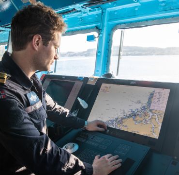 inne på broen i en fregatt. En mann står og ser på et sjøkart