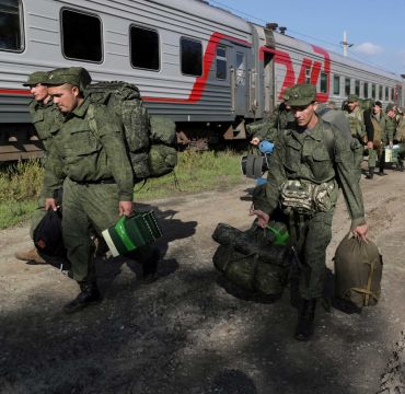 Russiske soldater i grønne uniformer bærer utstyr langs et parkert tog.