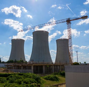 Tre gigantiske kjøletårn. En heisekran. Sol. Utendørs. Blå himmel.