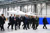 Menn i dress går rundt i en stor hangar med et moderne hvitt jagerfly i bakgrunnen