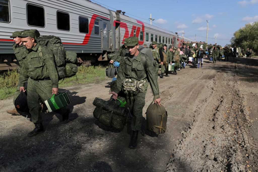 Russiske soldater i grønne uniformer bærer utstyr langs et parkert tog.