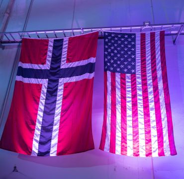 Det norske og amerikanske flagget henges side om side inne i en hall.