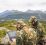 To militærkledde sitter med PC og radioutstyr på en fjellknaus i høstlandskap