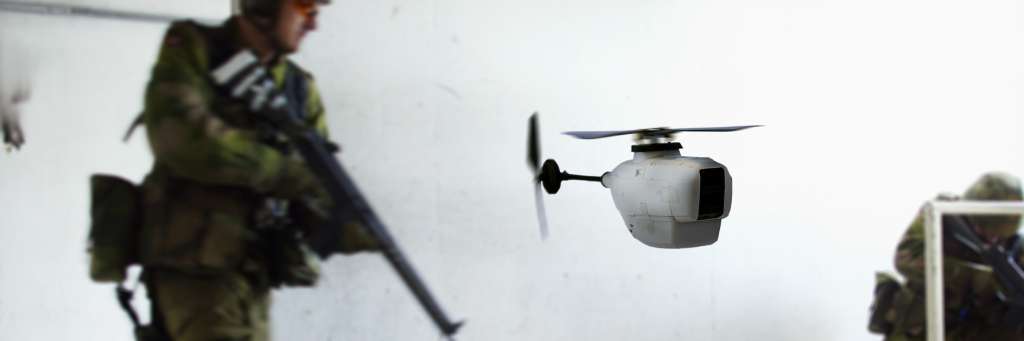 Liten drone i forgrunn, soldat med våpen i bakgrunn. Foto